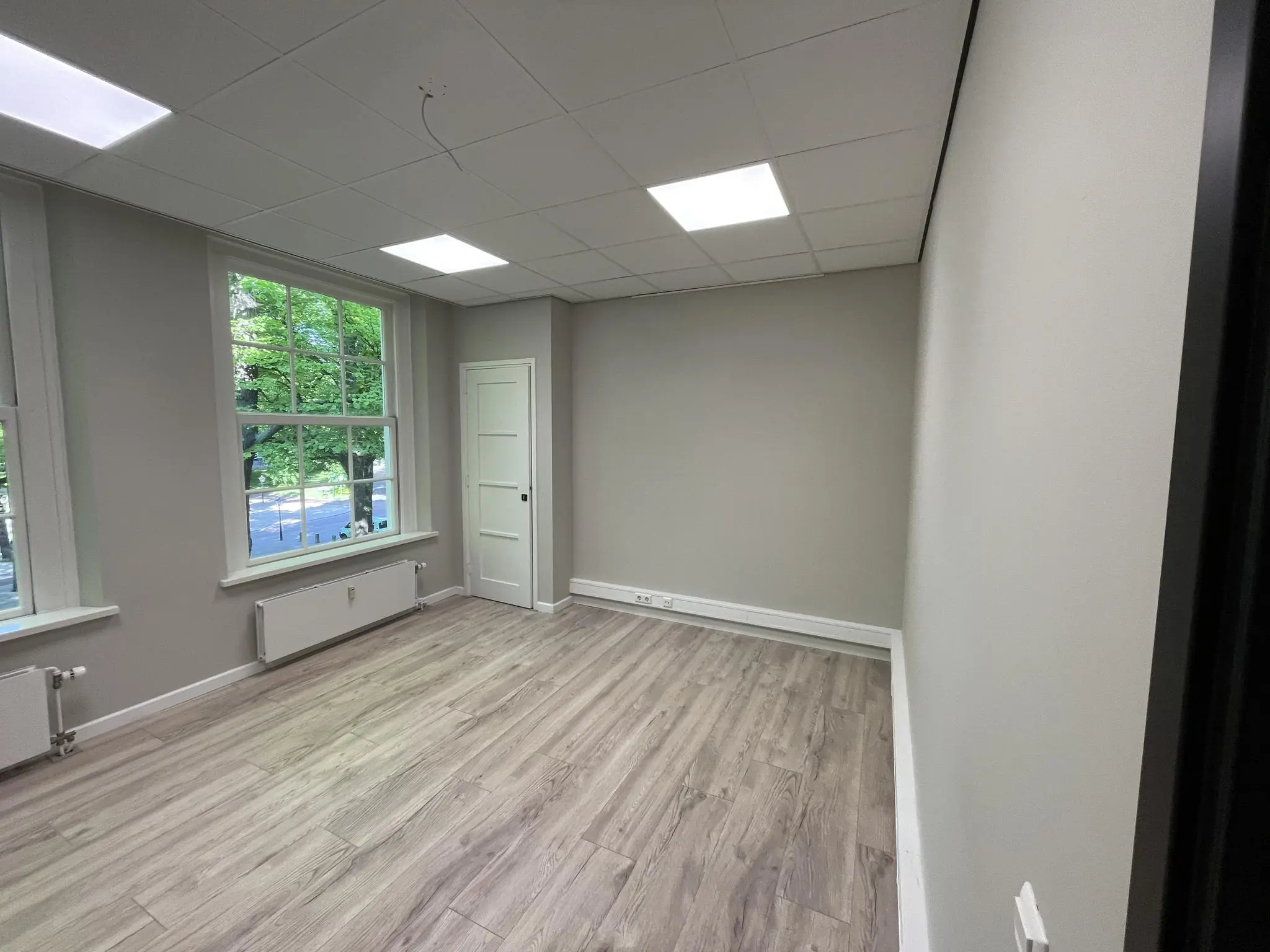 Licht kantoorruimte met houtlook vloer, grote ramen en zicht op de Lange Voorhout.